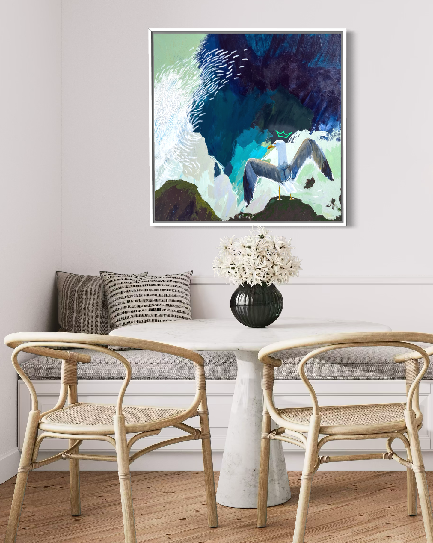 Framed abstract artwork of a crowned seagull with spread wings painted by New England artist Megan Carty, on a wall in a white kitchen banquette.