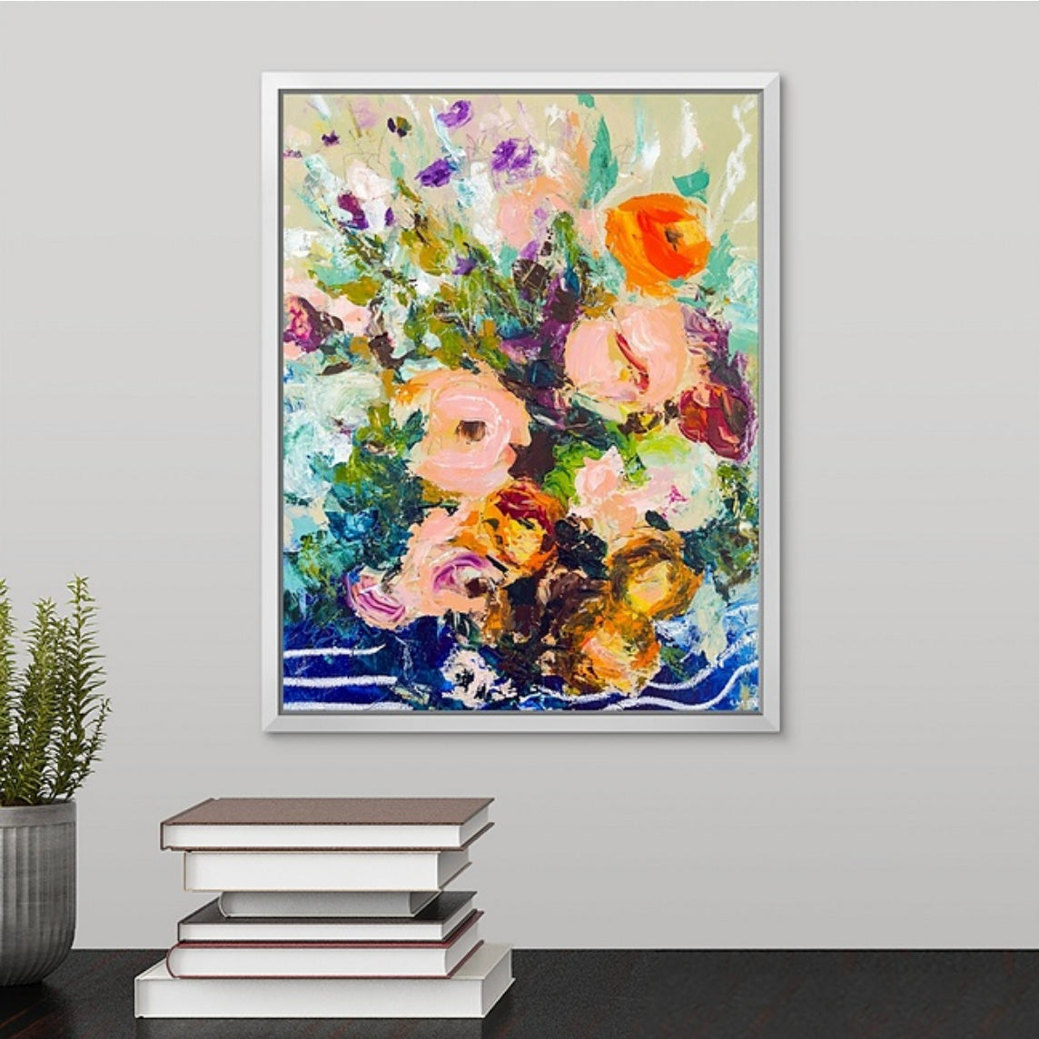 Framed abstract floral painting on a wall above a stack of books with a plant to the left. Painted by New England artist Megan Carty