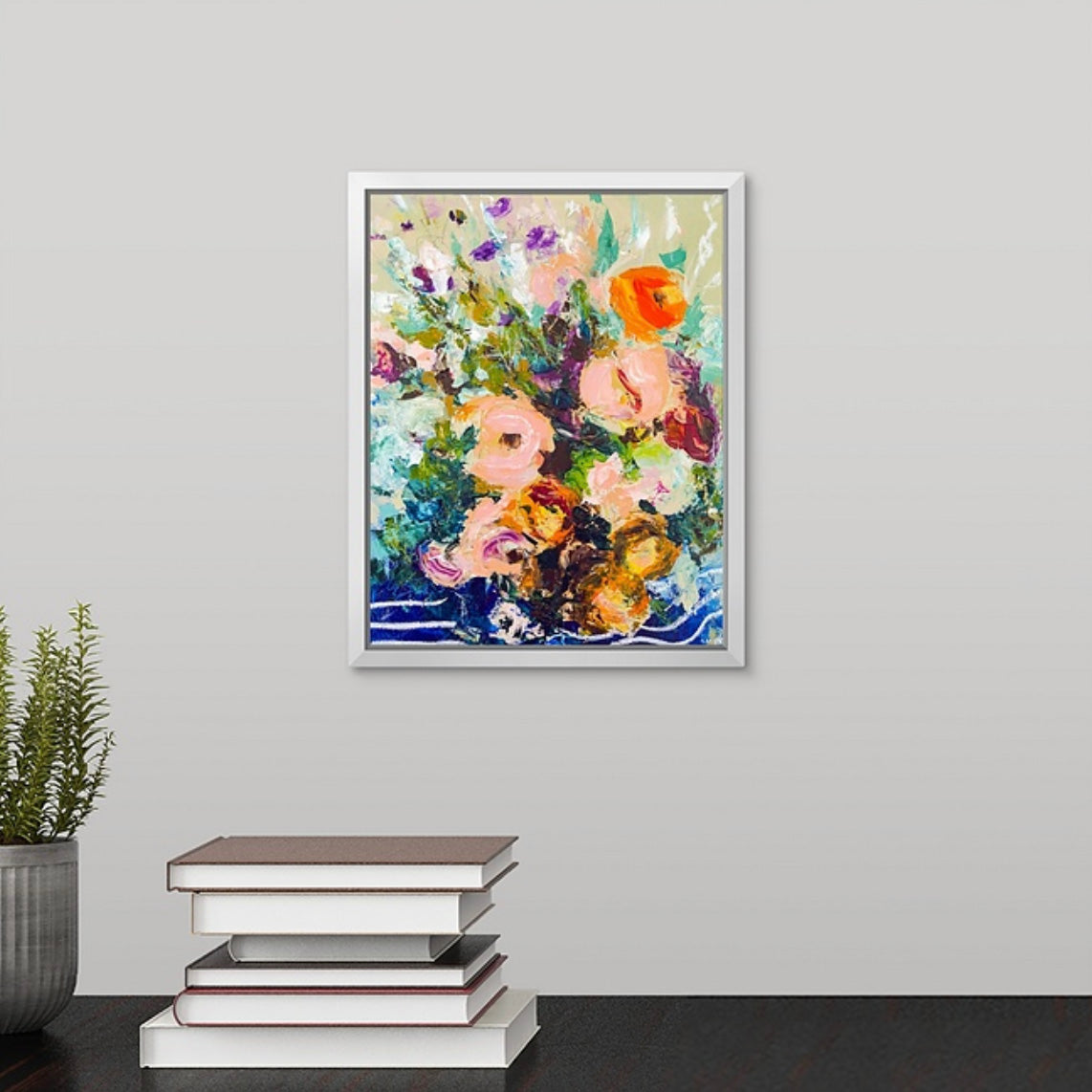 Framed abstract floral painting on a wall above a stack of books with a plant to the left. Painted by New England artist Megan Carty