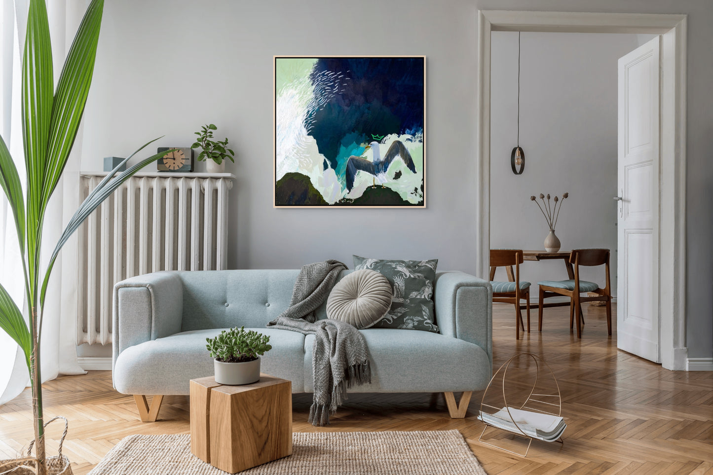 Framed abstract artwork of a crowned seagull with spread wings painted by New England artist Megan Carty, on a wall in a modern living room.
