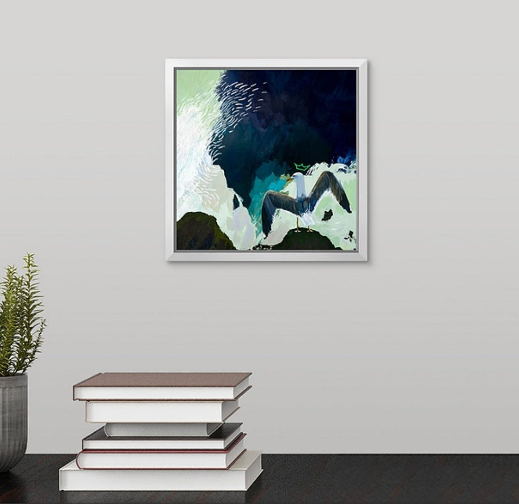 Framed abstract artwork of a crowned seagull with spread wings painted by New England artist Megan Carty, on a wall with books and a plant below.