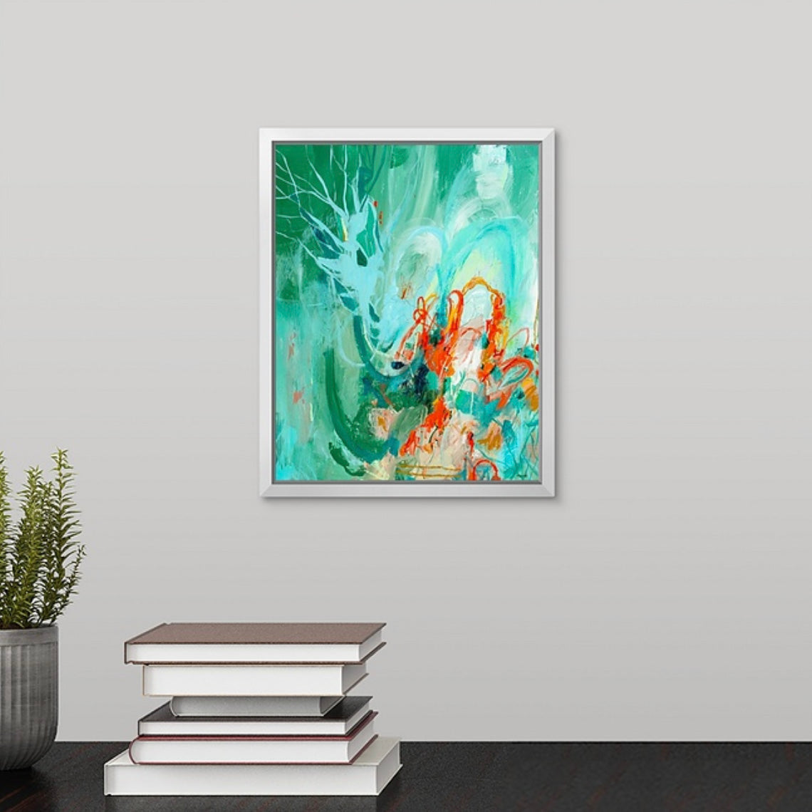 Framed abstract painting with green and orange colors on a gray wall above a stack of books.