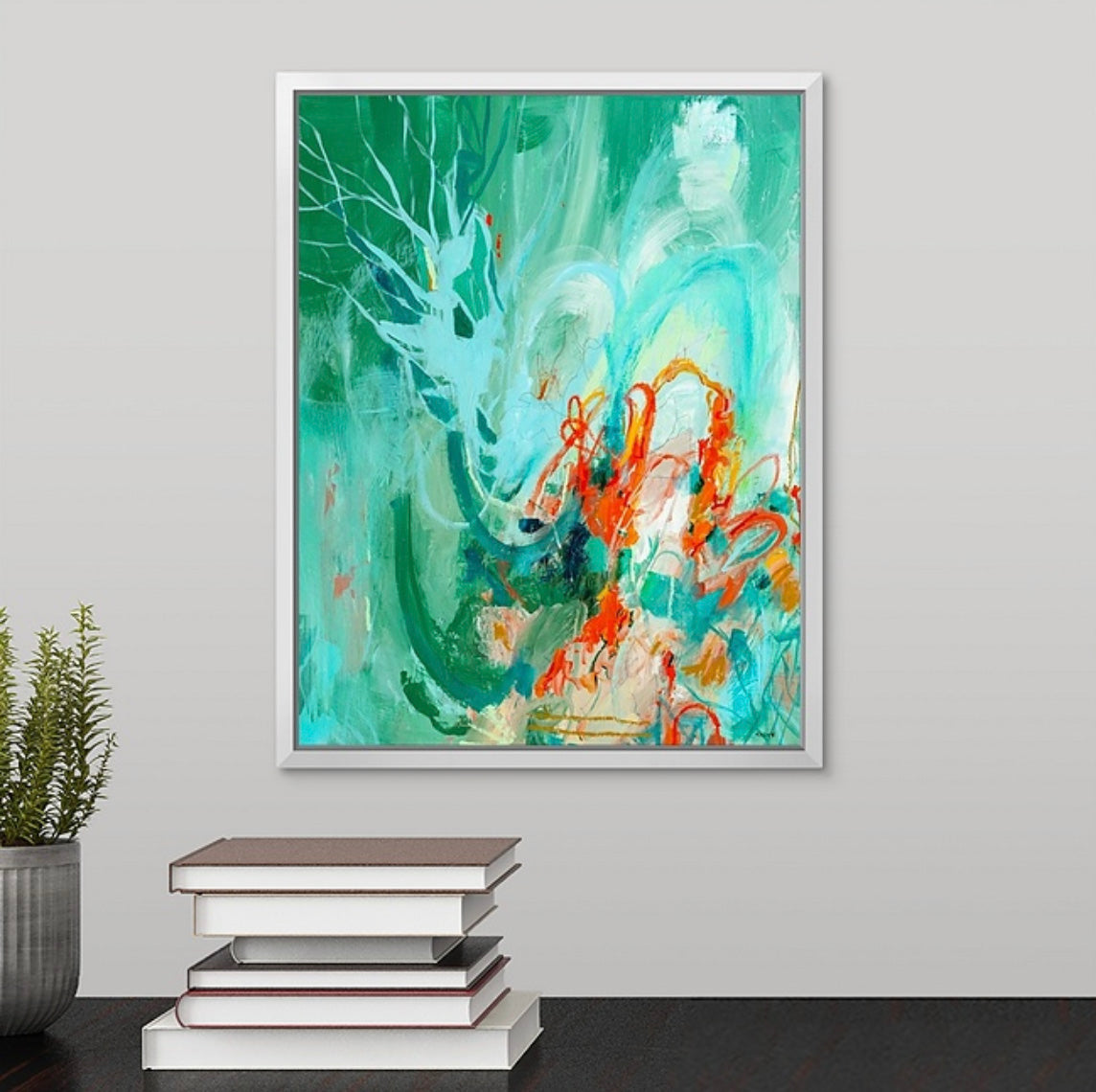 Abstract artwork by megan carty in a white frame on a gray wall with books and a plant below.