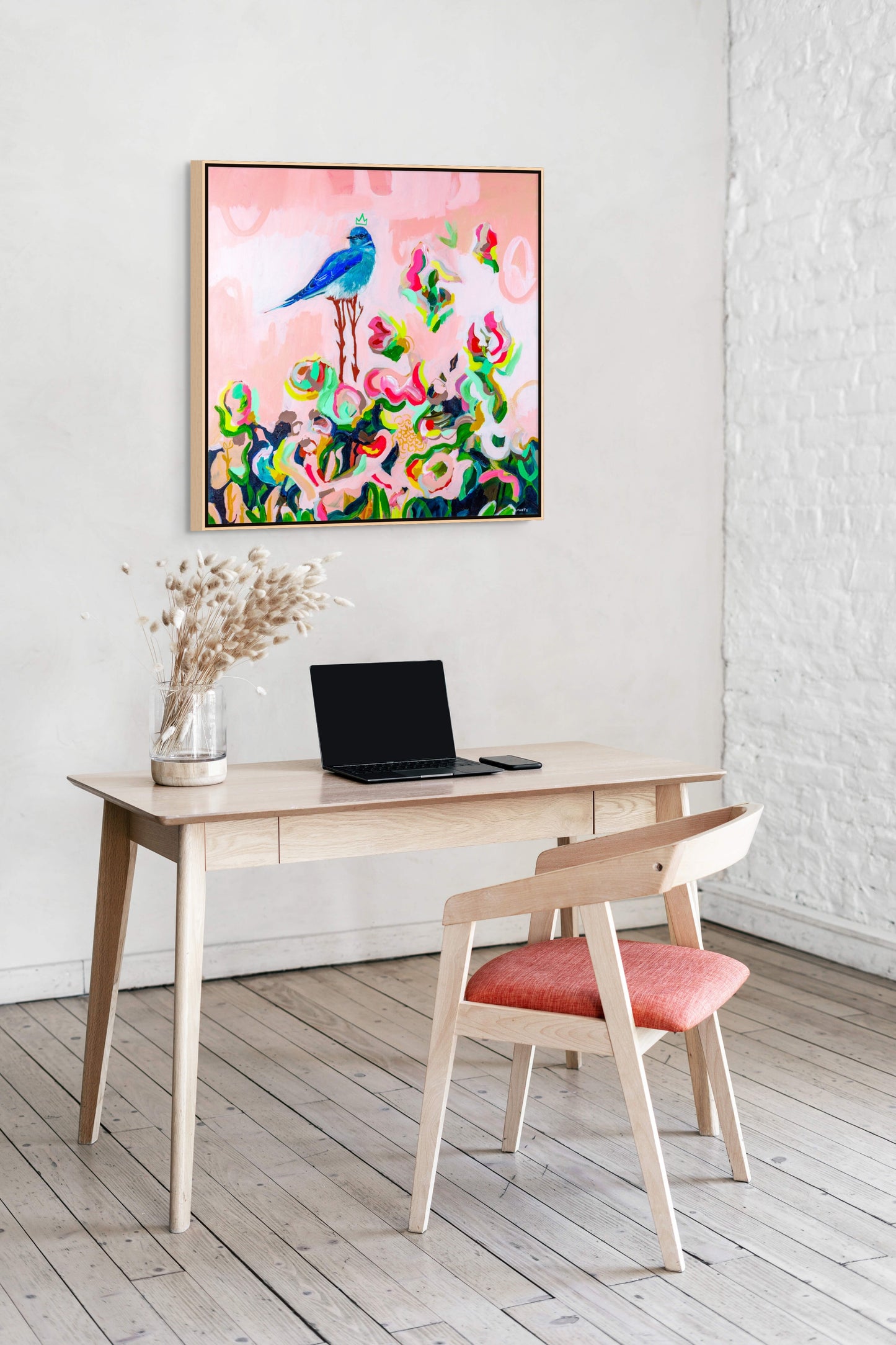 Framed abstract floral painting with a bluebird, painted by Boston area artist Megan Carty, hanging over a Scandinavian style desk with a laptop.