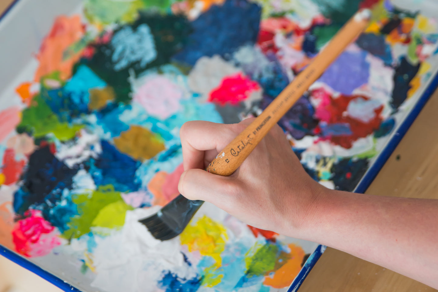 New England artist Megan Carty, holding a paint brush over a colorful palette of paint