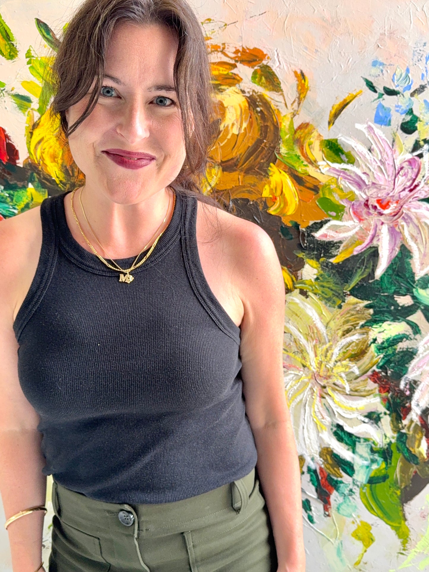 Megan Carty sitting in her studio with large abstract floral painting on the wall behind her.