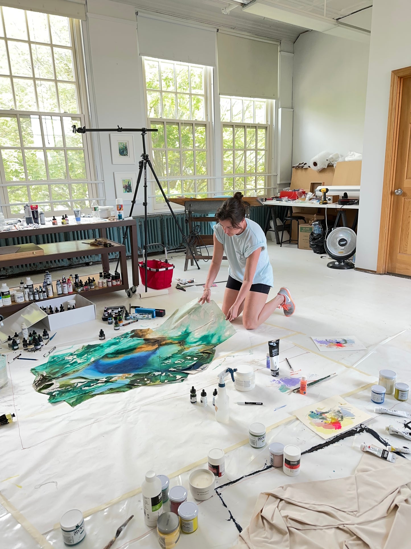 Groton, MA artist Megan Carty painting a large landscape on a table with various art supplies around.