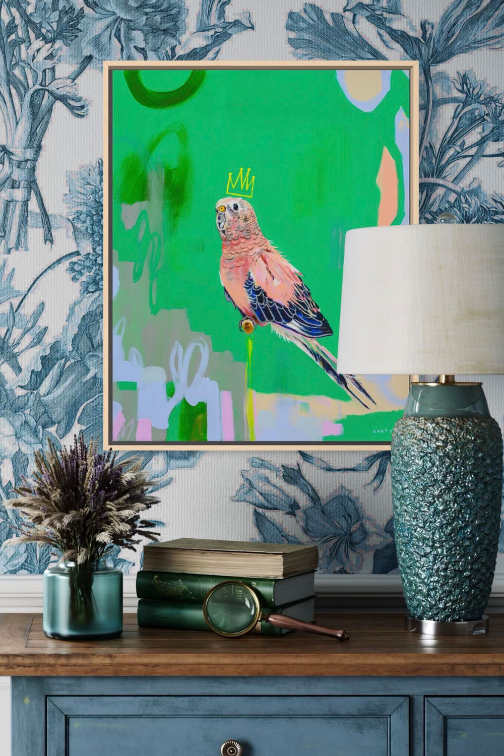 Framed artwork of a parrot on a wall with decorative items on a wooden surface below by Megan Carty