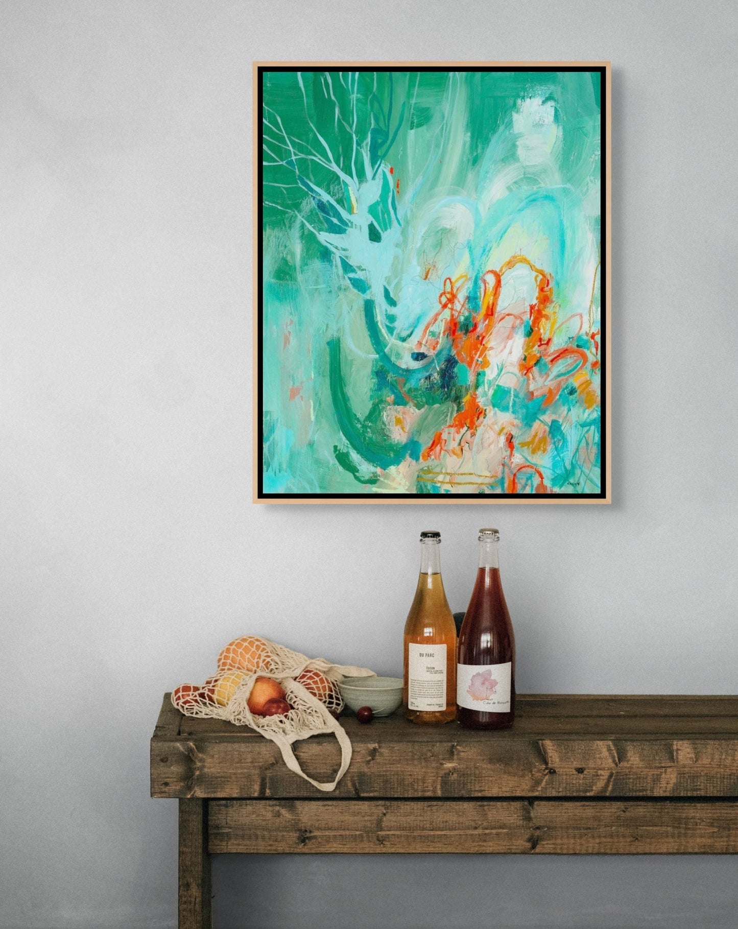 Framed abstract artwork on a gray wall above a wooden console table with bottles and fruit. By Groton, MA artist Megan Carty