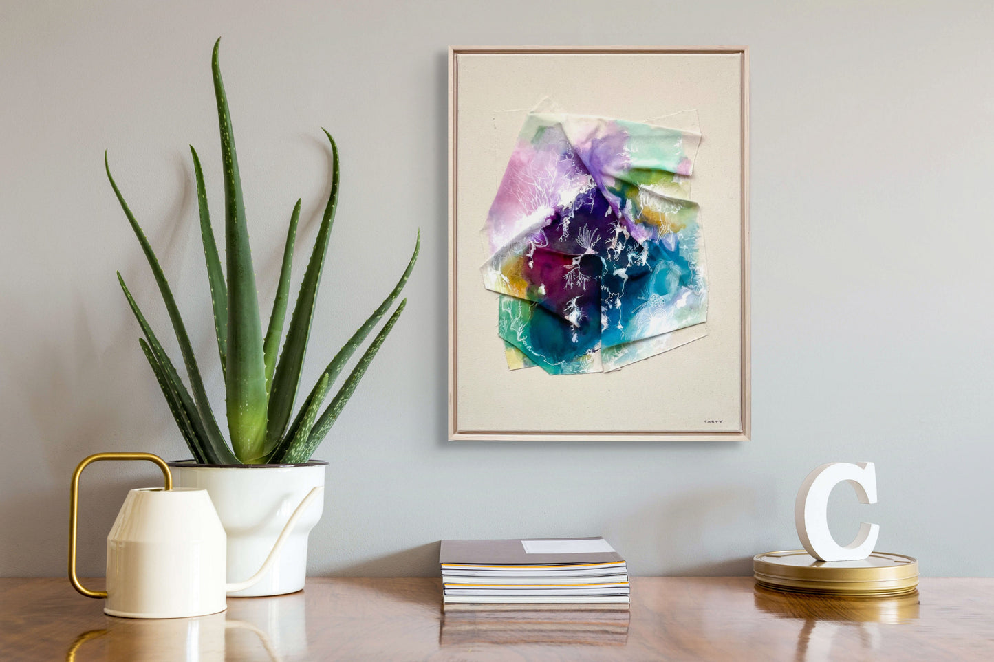 Colorful abstract landscape painting by New England artist Megan Carty on a wall above a table with decor items.