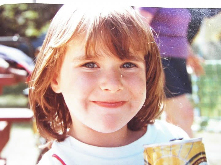 Artist Megan Carty as a young girl with a smile on her face outdoors, holding a countrytime lemonade can in 1984